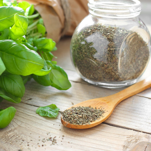dried basil in a glass container with a wooden spoon and fresh basil leaves