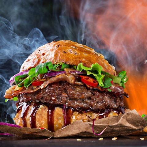 huge beef burger with bacon and salad in seeded bun with flames